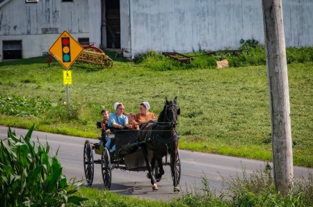 Téléchargez les photos : Ronks, Pennsylvanie, 19 juillet 2022 - Vue d'un cheval ouvert et d'un buggy avec deux femmes amies et trois enfants voyageant sur une route rurale un été lors d'une journée d'été - en image libre de droit