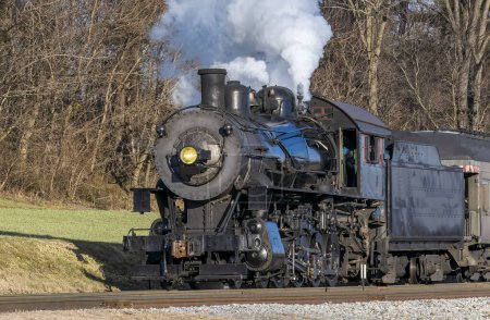 Téléchargez les photos : Une vue rapprochée d'une machine à vapeur antique soufflant de la vapeur tout en voyageant lentement à travers la campagne, un jour d'automne - en image libre de droit