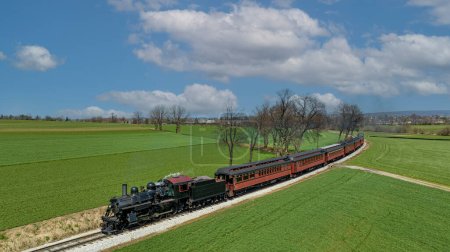 Téléchargez les photos : Un Drone Vue de face d'un train de passagers à vapeur antique approchant autour d'une courbe à travers des terres agricoles fertiles par une belle journée ensoleillée - en image libre de droit
