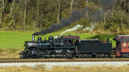 Photo for A Drone Side View of an Antique Steam Locomotive, Blowing Black Smoke on a Fall Day - Royalty Free Image