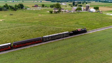 Foto de Un antiguo tren de pasajeros de vapor que viaja a través de tierras de cultivo, con cultivos plantados, soplando humo en un soleado día de primavera - Imagen libre de derechos