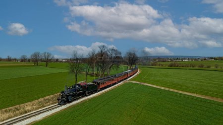 Téléchargez les photos : Un Drone Vue de face d'un train de passagers à vapeur antique approchant autour d'une courbe à travers des terres agricoles fertiles par une belle journée ensoleillée - en image libre de droit