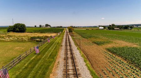Foto de Una vista aérea en una sola vía férrea con una valla con banderas de Estados Unidos en ella, en un día de verano - Imagen libre de derechos
