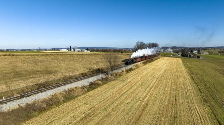 Foto de Una vista aérea de un tren de pasajeros de vapor acercándose, viajando a través de tierras de cultivo que soplan humo en un día de otoño - Imagen libre de derechos