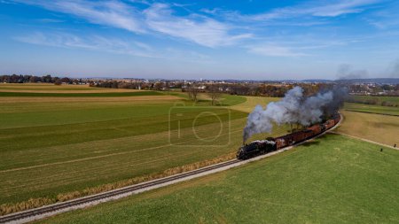 Foto de Una vista aérea de un tren de carga de vapor acercándose alrededor de una curva que sopla humo en un día soleado de otoño - Imagen libre de derechos