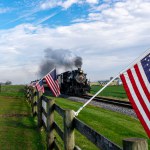 Ronks, Pennsylvania, November 4, 2023 - View of an Antique Steam Passenger Train Approaching With a Line of American Flags, Blowing Smoke on a Fall Day