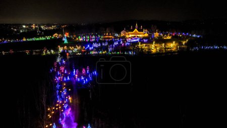 Foto de Vista aérea de una escena nocturna festiva con un rastro de humo púrpura que conduce a un castillo brillantemente iluminado rodeado de árboles coloridos. - Imagen libre de derechos