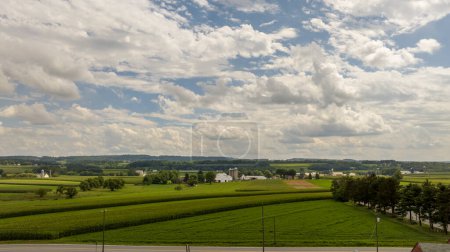 L'immensité des terres agricoles s'étend sous un ciel parsemé de nuages duveteux, résumant l'espace ouvert et la sérénité de la vie rurale.