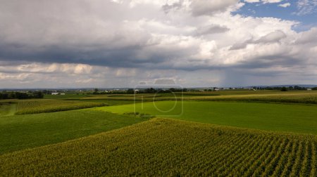Dramatische Gewitterwolken wälzen sich über einem Flickenteppich von Ackerland und unterstreichen das dynamische Zusammenspiel zwischen Wetter und Landwirtschaft.