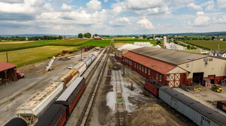 Photo for Strasburg, Pennsylvania, August 15, 2023 - An expansive view from above captures a rural rail yard with freight cars, surrounded by the lush, orderly farmlands stretching into the distance. - Royalty Free Image