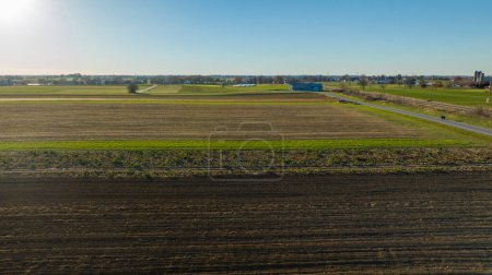 Sous un ciel bleu clair, cette image couvre les terres agricoles de banlieue et son mélange harmonieux de champs, idéal pour les concepts immobiliers et d'urbanisme.