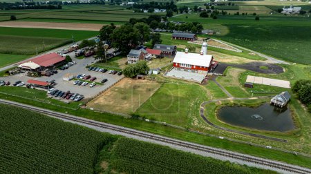 Photo for Ronks, Pennsylvania, August 15, 2023 - This vibrant aerial shot captures the active life of a rural complex, complete with a restaurant, parking, and a serene pond set against a backdrop of extensive - Royalty Free Image