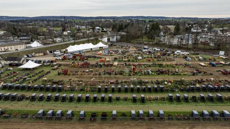 A bustling rural auction comes to life in this overhead shot, capturing rows of Amish buggies and an array of agricultural equipment on sale.