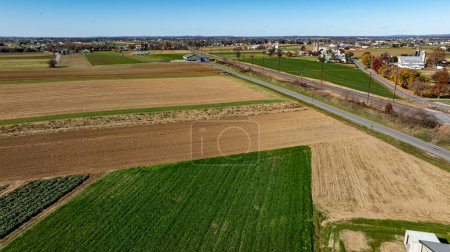 Eine ausgedehnte Drohnen-Erfassung von Ackerland entlang einer Landstraße, die eine Mischung aus brachliegenden und grünen Parzellen zeigt, geeignet für Diskussionen über ländliche Entwicklung und Landnutzung.