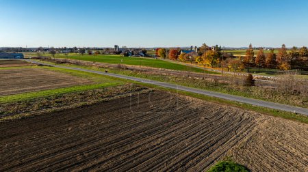 Eine Luftaufnahme fängt das strukturierte Ackerland im Herbst ein, mit einer durchschneidenden Landstraße, perfekt für saisonale landwirtschaftliche und ländliche Themen.