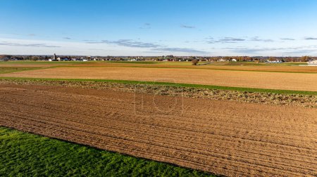 Photo for Late afternoon light bathes a patchwork of harvested and plowed fields in a rural landscape, symbolizing the end of a farming cycle. - Royalty Free Image