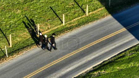 Foto de Ronks, Pennsylvania 14 de noviembre de 2023 - Un trío de amish, caminata por un camino rural, proyectando largas sombras bajo el sol de la tarde, perfecto para el estilo de vida y los temas comunitarios. - Imagen libre de derechos