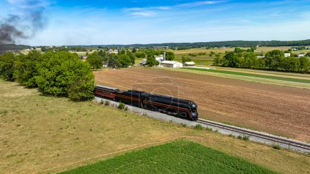 Photo for An evocative aerial view of a steam train puffing through picturesque rural farmlands, marked by vividly colored fields and pastoral settings. - Royalty Free Image