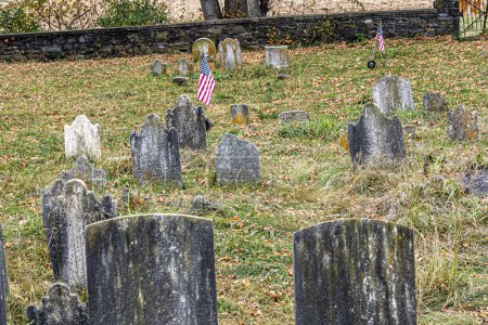 Imagen conmovedora de un antiguo cementerio con lápidas erosionadas y banderas americanas, enclavado entre hojas caídas de otoño, mostrando un solemne homenaje al pasado.