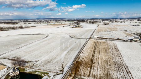 An Aerial View Of Expansive Snow-Dusted Farmland With Rural Buildings And Silos.