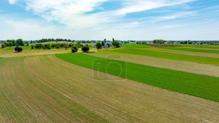 Blick aus der Vogelperspektive auf eine ausgedehnte ländliche Landschaft, mit sauber geteilten grünen und gepflügten Feldern neben landwirtschaftlichen Gebäuden, die das Wesen der Landwirtschaft zusammenfassen.