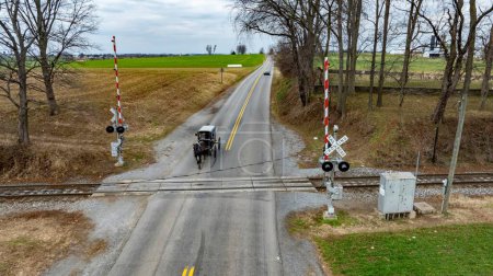 A Rural Road with An Amish Horse-Drawn Carriage at Railroad Crossing