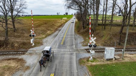 A Rural Road with An Amish Horse-Drawn Carriage at Railroad Crossing