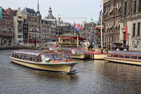 Foto de Ámsterdam, Países Bajos - 31 de marzo de 2017: Barcos turísticos en un canal y personas caminando por casas históricas en Ámsterdam, Países Bajos en marzo 31, 2017 - Imagen libre de derechos