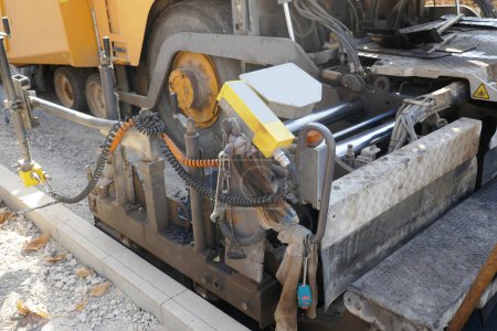 Foto de Una máquina de pavimentación que coloca asfalto fresco o betún sobre una base de grava durante la construcción - Imagen libre de derechos