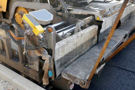 Foto de Una máquina de pavimentación que coloca asfalto fresco o betún sobre una base de grava durante la construcción - Imagen libre de derechos