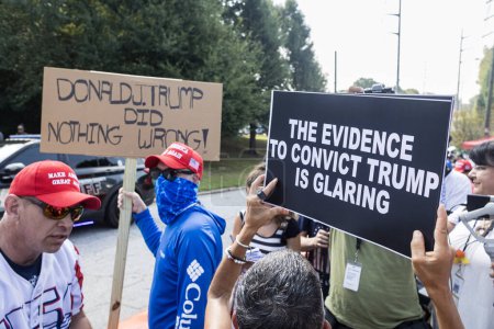 Foto de Atlanta, GA / Estados Unidos - 24 de agosto de 2023: Un hombre sostiene un letrero que dice "Donald J. Trump no hizo nada malo" junto a una mujer que sostiene un letrero que dice "La evidencia para condenar a Trump es evidente" fuera de la cárcel del condado de Fulton el 24 de agosto de 2023 en Atlanta, GA. - Imagen libre de derechos
