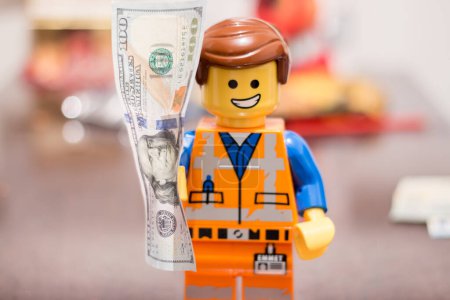 Foto de Slovakia. Sala. 01/01/2023. Banknote in the hands of a LEGO worker, with a joyful expression on his face.. Money in the hands of Lego Movie 2 Emmet Smile. - Imagen libre de derechos