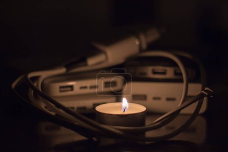 A burning candle against the background of power banks and a charger. Blackout due to war in Ukraine