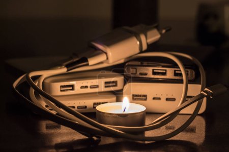 A burning candle against the background of power banks and a charger. Blackout due to war in Ukraine