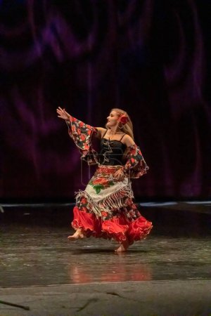 Foto de Una chica con un vestido nacional baila un baile gitano en el escenario - Imagen libre de derechos