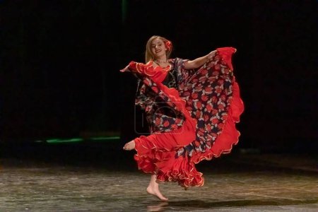 Foto de Una chica con un vestido nacional baila un baile gitano en el escenario - Imagen libre de derechos