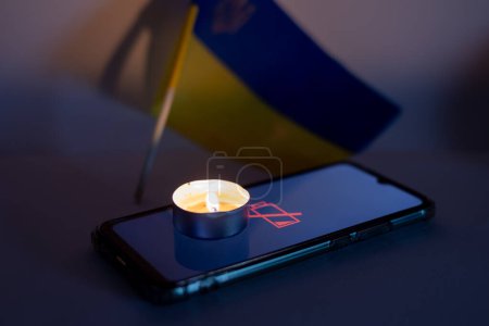 A burning candle and a discharged mobile phone against the background of the Ukrainian flag