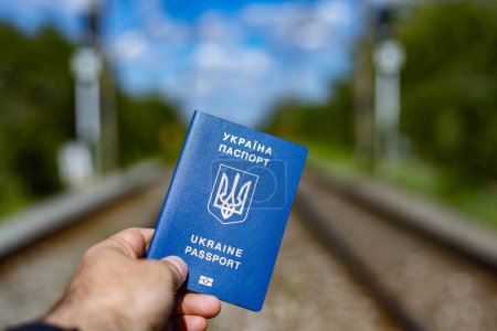 Ukrainischer Pass in den Händen eines Mannes auf dem Bahngleis. Männer verlassen das Land en masse, weil ihr Leben in Gefahr ist