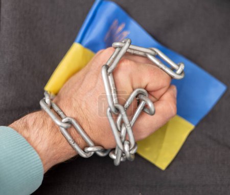 A man's hand entangled in a chain and the flag of Ukraine. Ban on citizens leaving the country