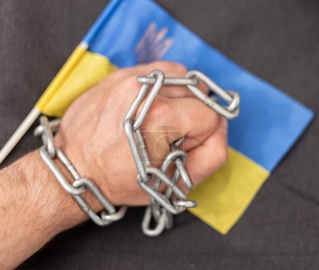 A man's hand entangled in a chain and the flag of Ukraine. Ban on citizens leaving the country