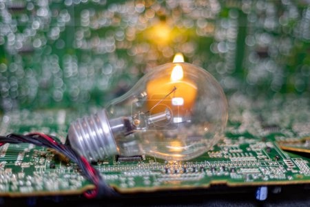 An incandescent lamp against the background of a burning candle and electronic circuit boards. Blackout due to the war in Ukraine