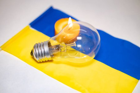 Light bulb on the background of a burning candle and the Ukrainian flag. Blackout due to the war in Ukraine