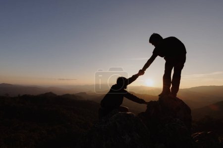 Photo for Silhouettes of two people climbing on mountain and helping. Help and assistance concept. - Royalty Free Image