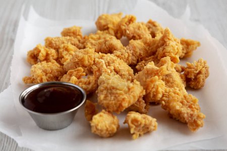 Homemade Popcorn Chicken with BBQ Sauce on a white wooden background, side view.