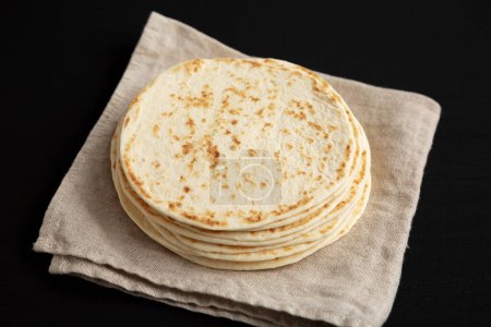 Stack of Whole Wheat Flour Tortillas on a black background, side view.