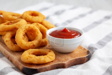 Photo for Homemade Crispy Deep-Fried Onion Rings with Ketchup on a rustic wooden board, low angle view. Close-up. - Royalty Free Image