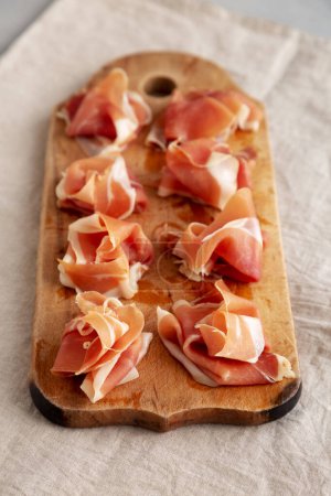 Slices of Appetizing Jamon Serrano Ready to Eat on a rustic wooden board, side view.