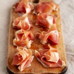 Slices of Appetizing Jamon Serrano Ready to Eat on a rustic wooden board, side view.