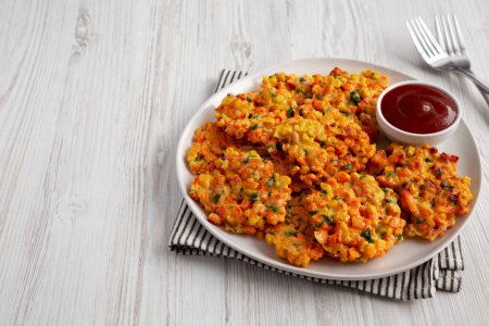 Téléchargez les photos : Beignets de maïs aux carottes faits maison avec ketchup sur une assiette, vue latérale. Espace de copie. - en image libre de droit