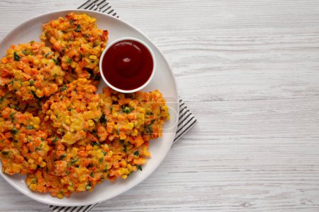 Téléchargez les photos : Beignets de maïs aux carottes faits maison avec ketchup sur une assiette, vue sur le dessus. Couché à plat, au-dessus, par le haut. Espace de copie. - en image libre de droit
